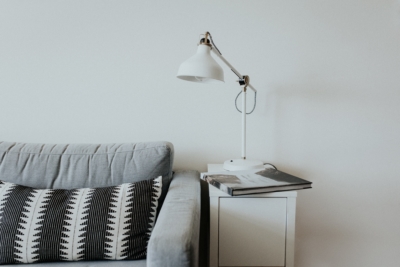 A gray couch with a white lamp and white table
