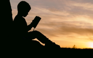 Child reading a book outside at sunset