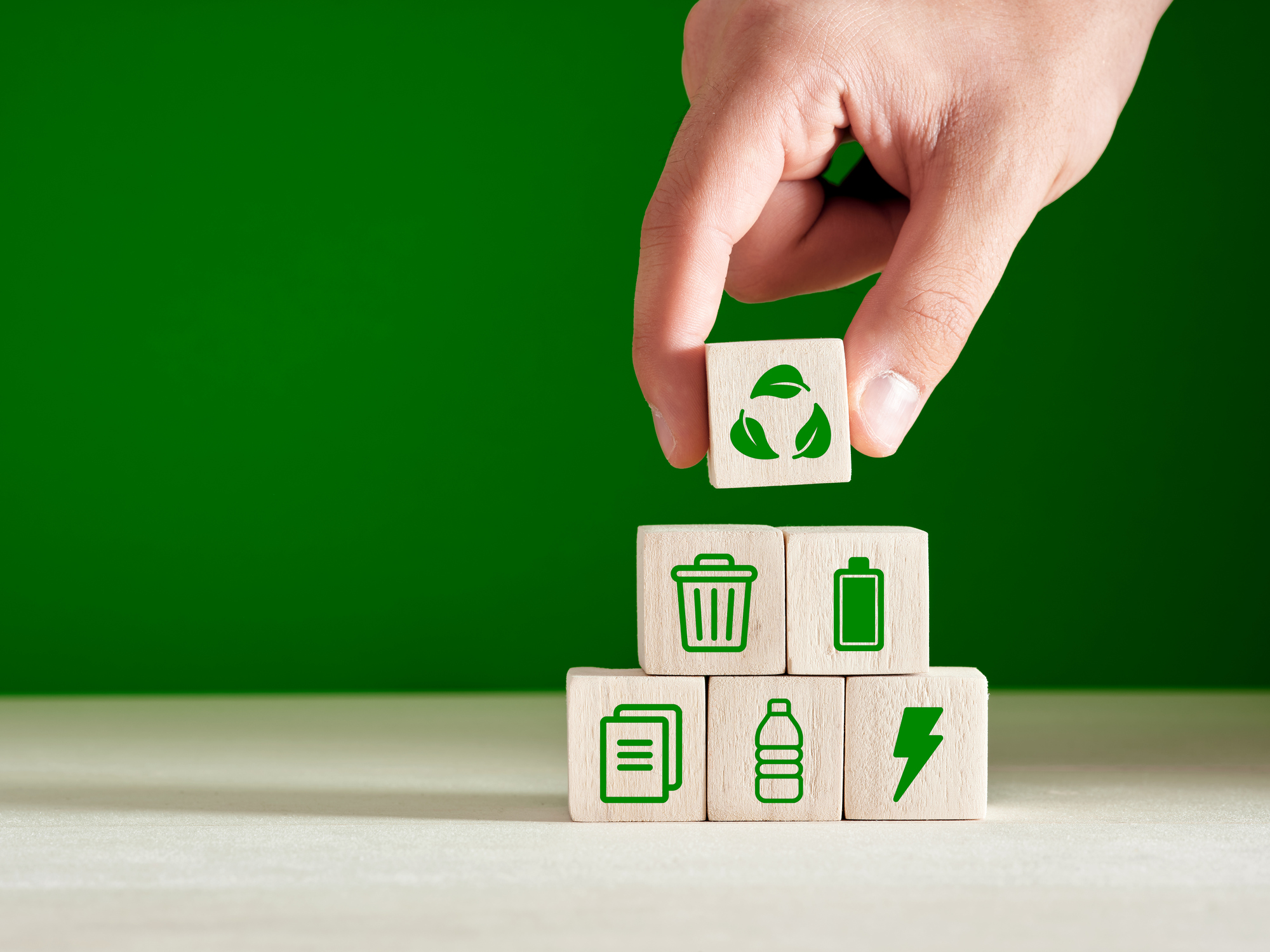 Recycling and environmental protection concept. Environment sustainable development. Hand puts recycling product material symbols on green background.